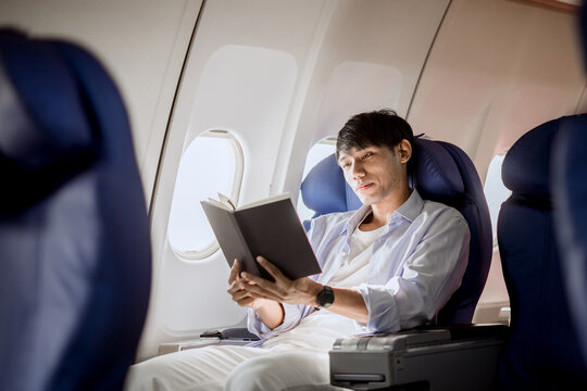 A businesswoman relaxes in her airplane seat, finding satisfaction and quiet contemplation while reading literature during a long vacation flight.