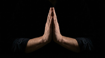 Close up of male hands clasped in prayer or namaste gesture on black background. Spiritual meditation and faith concept with copy space