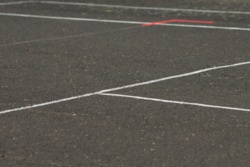 white court lines crossing dark asphalt surface with faint red accent in distance, empty outdoor playground scene, intersecting boundaries
