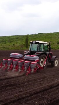 Agricultural tractor with seed drill is actively planting seeds in a plowed field, showcasing the planting process and soil disturbance as the machine moves forward