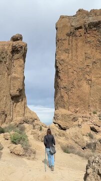 Roque Nublo: Hiker walking on a mountain trail towards a gap between two giant volcanic rock formations. Gran Canaria.