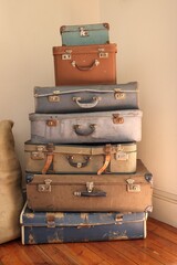 Stack of seven old, pastel colored, well worn, suitcases in corner. Nostalgia, interior decoration and travel. Front view