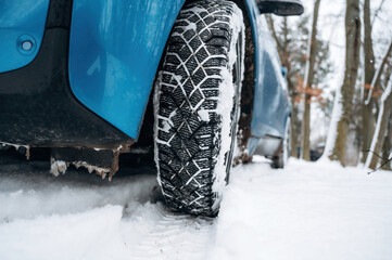 Close-up of a winter tire on a blue vehicle, showcasing tread patterns in snow-covered terrain, emphasizing traction and winter driving conditions for safety and performance