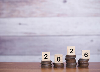 Wooden blocks with the number 2026 and plants growing up on stack of coins. The concept of saving money, Financial, Investment and Business growing in year 2026.