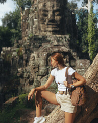 Fototapeta premium Female Traveler Resting By Ancient Bayon Temple Stone Face In Cambodia Jungle