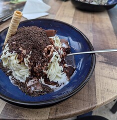 Close-up of a blue plate with a delicious spaghetti ice cream topped with chocolate sprinkles and a wafer roll on the side
