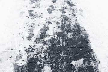 Slippery sidewalk with snow and footprints. Icy pavement in winter city. Trampled snow on dark asphalt path. Cold weather walking conditions. Risk of slipping outdoors. Urban winter ground texture.