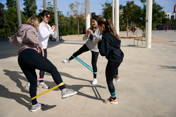 Four women training with resistance bands outdoors