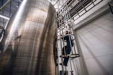 Top view male worker climbs up the ladder inspection stainless tank work at height