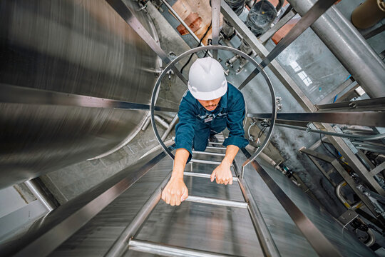 Top view male worker climbs up the ladder inspection stainless tank work at height