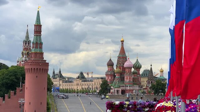 RUSSIA, MOSCOW - June 13, 2025: The Moscow Kremlin with Russian flags fluttering in the wind on a cloudy day, and bright flowers in the flowerbeds. The tricolor is framed by St. Basil's Cathedral. 4К