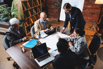 Senior Indian Asian executives reviewing plans and drawings together at modern office desk