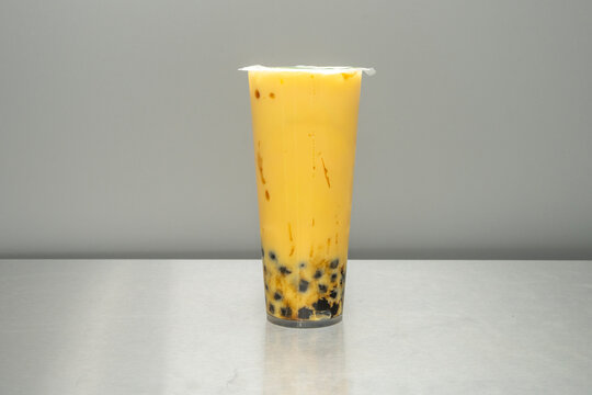 A glass of passion fruit bubble tea, with numerous black seeds suspended in a translucent yellow liquid and a wide straw ready to be inserted through the sealed lid