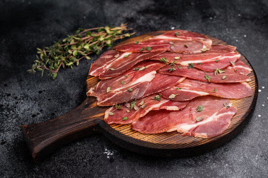 Slovenian ham, sliced cured pork meat on wooden board, Prsut. black background. top view
