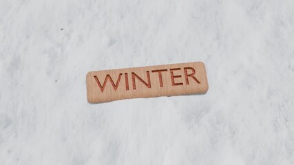 Winter Text Engraved on Wooden Block Lying on Snow. Wooden Plaque in Snow. 4K