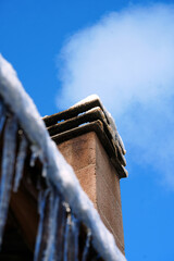 Smoking chimney on a snowy roof with icicles under blue sky