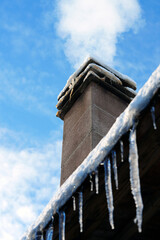 Smoking chimney on a snowy roof with icicles under blue skySmoking chimney on a snowy roof with icicles under blue sky