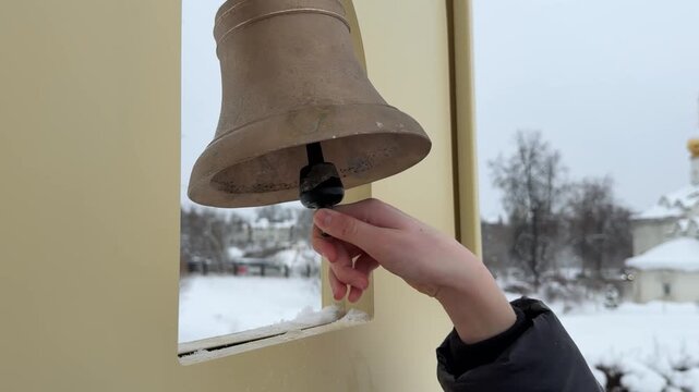  Hand Ringing Large Brass Bell in Outdoor Setting.Close-up image of a hand ringing a large brass bell outside. The bell is prominently displayed, with the hand gripping the clapper. 