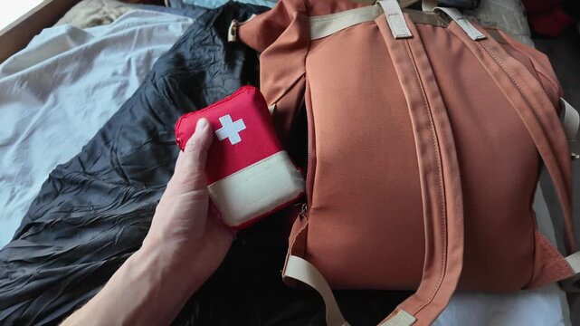 Hand Removes Small First Aid Pouch From Backpack Before Departure. CloseUp Shows Zipper Pull And Strap Details Readying Compact Medical Kit For Trail And Outdoor Emergency Response