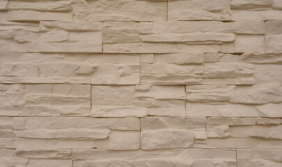 A flat wall surface covered with decorative cream color gypsum tiles that look like stone
