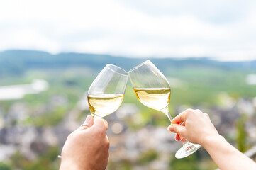 Zwei Weingläser mit Weisswein stoßen an mit weichen Mosel Bokeh im Hintergrund