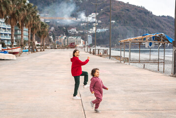 Two children in colorful clothes joyfully running and playing on a wide seaside promenade with mountains in the background, symbolizing the concept of carefree childhood and freedom