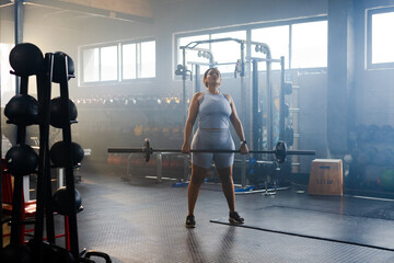 Female performing barbell lift at gym on rubber flooring, wearing light blue workout gear