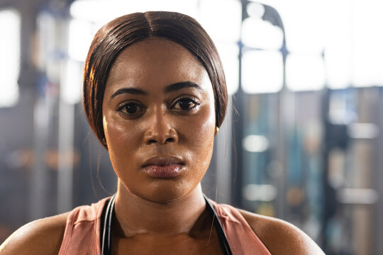 African American woman training and sweating in gym with dusty-rose tank top and blurred weights