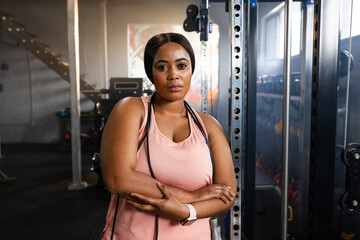 Mid-adult African American woman standing in gym near cable machine wearing pink top with jump rope
