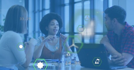 Center woman in brown overall dress speaking, gesturing at office table, with laptop and overlays