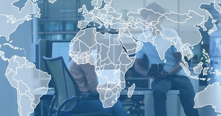 Collaborating duo wearing casual attire at desk, using tablet and monitors with world map graphic