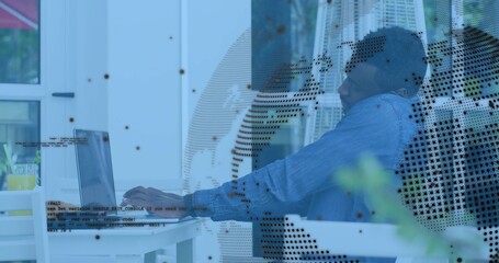 Man in blue denim shirt typing on laptop by glass doors, with drink, heater, globe overlay