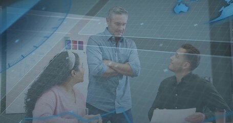 Standing senior manager in blue shirt leading team at meeting table, with whiteboard and papers