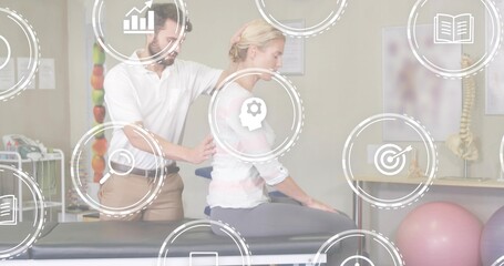 Treating clinician in white polo applying manual therapy to patient on table in rehab, spine model