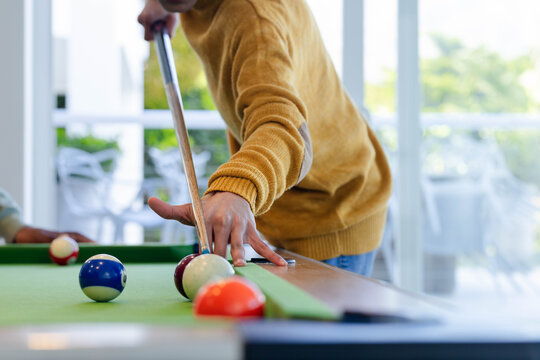 Two men including mustard-sweater man leaning over green-felt pool table lining up cue at home