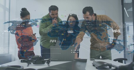 Analyzing team in orange tan attire pointing at laptop at office table, with drone, projected map