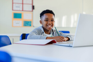 African American schoolboy working at school desk in grey hoodie, with pencil and red notebook