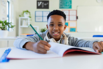 African youth male student writing with green pencil in classroom at desk with white headphones