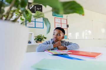 African male youth in light gray sweatshirt, sitting at white table in classroom studying notebooks