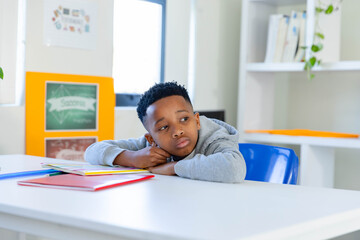 Adolescent African American male student sitting on blue chair at class table with colorful folders