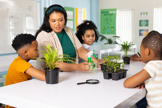 African American teacher with three kids showing plant care in classroom holding green spray bottle