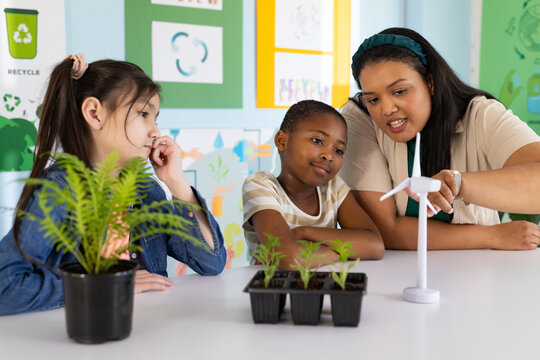 Diverse teenage students and teacher pointing at wind turbine while watching plants in classroom