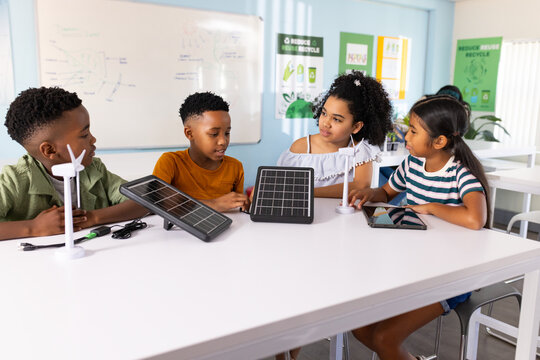 Diverse youth students assembling and testing solar panels and wind turbines at school with tablet