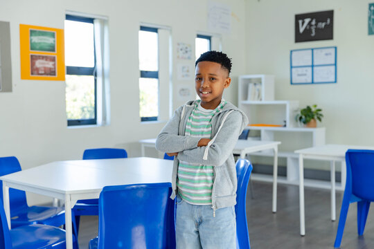 African American male student standing with arms crossed at school in hoodie and jeans near windows