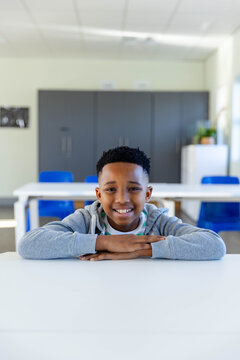 African American youth male sitting at white classroom table wearing light gray hoodie and lanyard