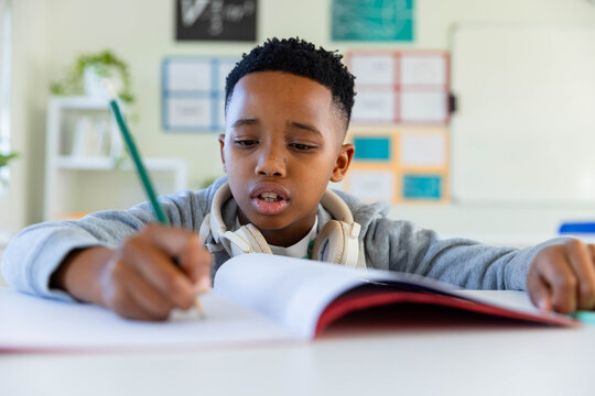 Preteen African American boy writing in workbook at low desk with green pencil and headphones