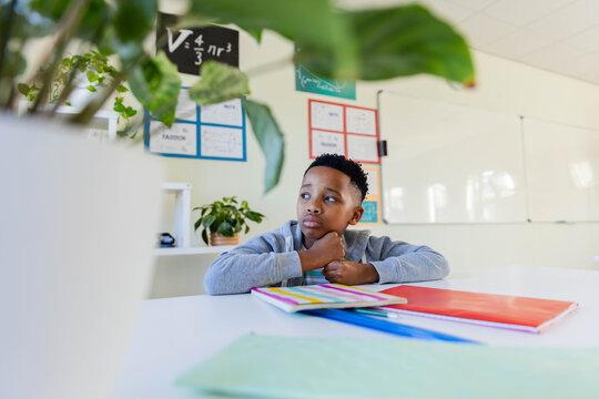 African male youth in light gray sweatshirt, sitting at white table in classroom studying notebooks