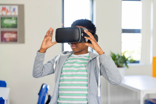Black VR headset resting on white classroom table near windows, with blue chairs and posters