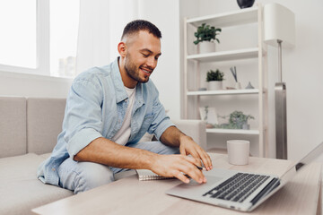 Smiling man working on laptop from home, reflecting modern remote work culture and embracing...