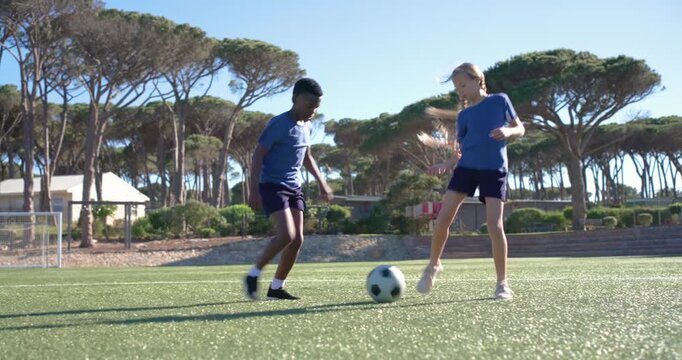 Defender approaching, two teens are exchanging close dribbles and tackles on turf to train skills